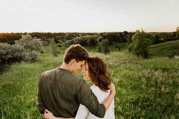 Young beautiful woman and man hug, kiss and walk in nature at sunset.