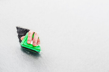 A hand with a plastic scraper cleans the windshield from ice and snow in winter - copy space