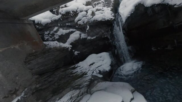 Water From Cascade du Rouget Flowing In The Stream With Coniferous Forest Covered With Snow In Winter. - FPV, aerial