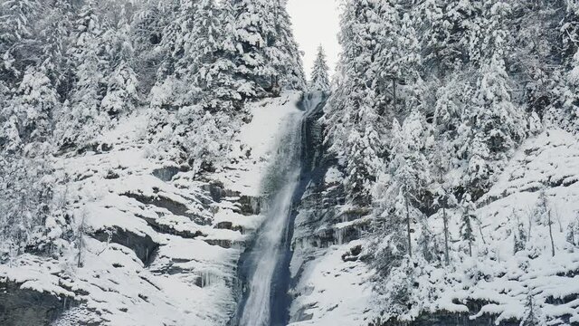 White icy forest waterfall of Cascade du Rouget, France in winter -tilt down