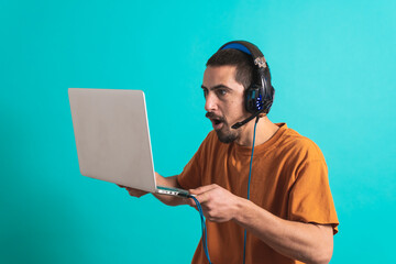 Young handsome man with gamer headphone set isolated over blue background using laptop computer...