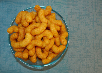 peanut flips . lots of corn sticks in peanut glaze in a glass round bowl on a blue textured background top view . calorie food