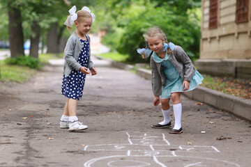 Two little girlfriends in blue dress and pigtails on her head playing hopscotch in the yard