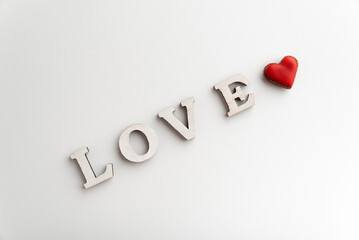 White inscription LOVE on white background and small red heart. Valentines day