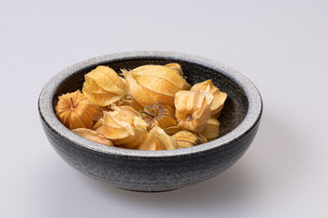 dry ground cherries in handmade rustic bowl on white background