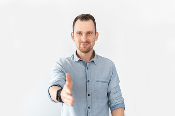 A smiling guy in blue smart casual shirt holds out his hand in handshake gesture, greeting, sign of good deal isolated on white