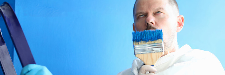 Portrait of construction site worker smelling paintbrush with blue paint. Professional repairman...