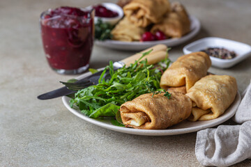 Homemade stuffed thin pancakes or crepes with meat, spicy cranberry sauce and arugula, light stone background. Traditional Russian cuisine for Maslenitsa. Shrove Tuesday.