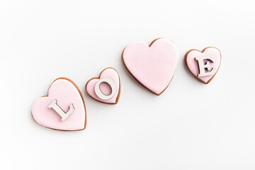 Gingerbread cookies in heart-shaped with white sugar icing on white background and inscription LOVE.