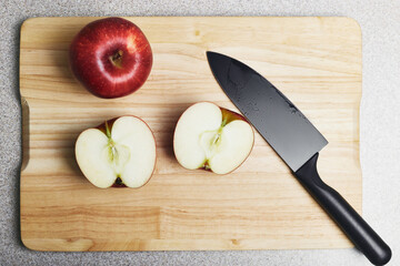 Cutting board with two red apples and a knife on it. One apple is whole, another one is cut, ready for cooking. Culinary class in a kitchen.