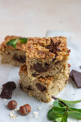 Oatmeal squares with chocolate, nuts, pieces of chocolate and mint, light concrete background. Diet bars. Healthy bakery for breakfast or dessert.