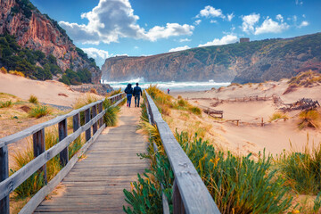 Torists walking to Cala Domestica beach on wooden pier. Windy summer scene of Sardinia, Italy,...