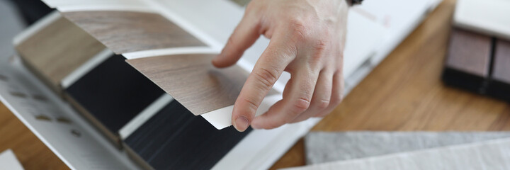Close-up of person choosing proper variant of material for apartment renovation. Desktop with colourful palette samples and laminate floor examples. Construction site and interior design concept