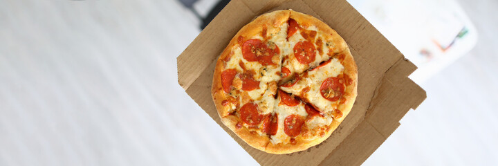 Top view of male person holding delicious pizza on hand. Round shaped lunch with tasty ingredients. Aromatic unhealthy food. Quick brunch at work in cabinet. Traditional italian meal