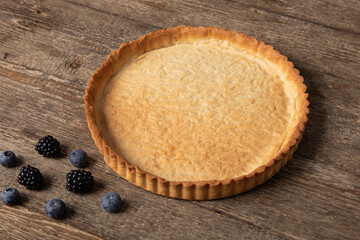 Top view of empty tart shell decorated with berries on wooden table 
