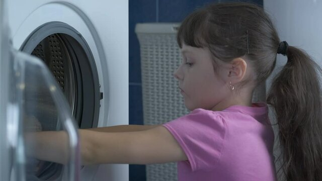 Load things in a washing machine. Little girl puts soft toys washing machine.
