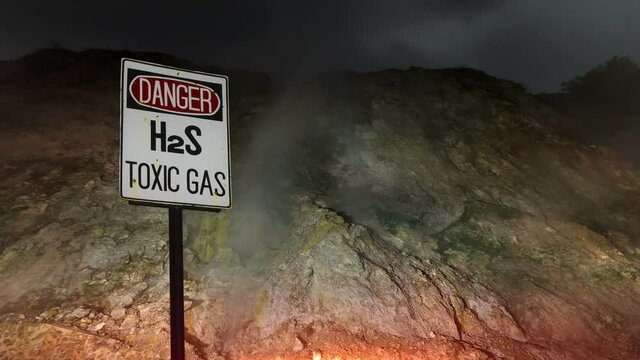 Smoke (sulphur) coming from volcanic hot springs at night time and sign Danger!