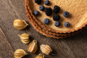Top view of empty tart shell decorated with berries and dried fysalis on wooden table 