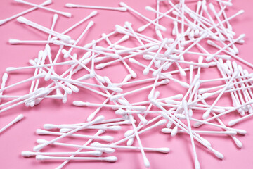 White cotton ear buds on a pink background.