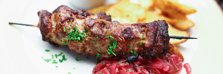 Close-up of delicious fresh baked meat and crusty potato served on white plate. Tasty dish decorated with greenery. Red yummy sauce. Portion for one. Food and healthy eating concept
