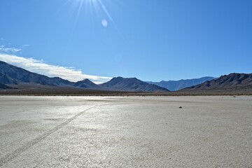 Fototapeta premium moving stones on the Racetrack Playa leaving tracks in the dry and cracked terrain in the Death Valley National Park, recflections of the sun