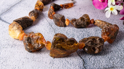 Unique rare  necklace made of natural old dark orange and green amber stones close up on a gray surface. Amber includes ancient plant and flowers.