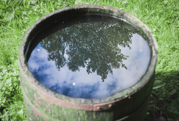 Fototapeta premium Old moss-covered barrel which reflects the sky, trees and lanterns