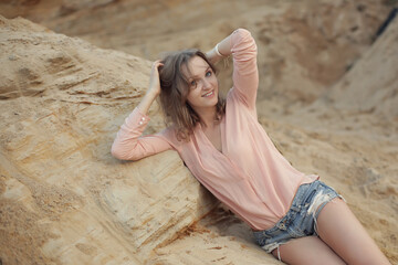beautiful girl in a pink blouse and denim shorts lying on the sand in the mountains