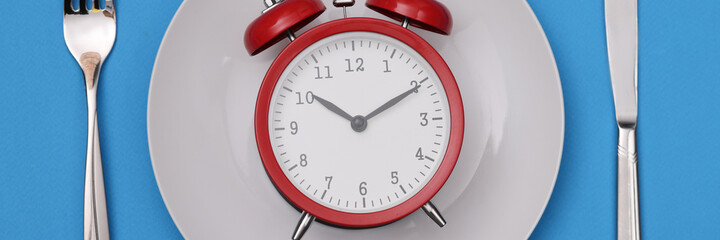 There is a red alarm clock on white plate. Diet regimen and healthy lifestyle concept
