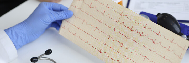 Doctor's hands hold result of the cardiogram next to patient sitting. Examination of the cardiovascular system concept.