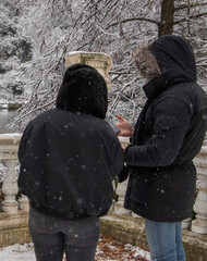 two friends enjoying the view of a lake of ducks with a big jugs and trees in a cold winter...