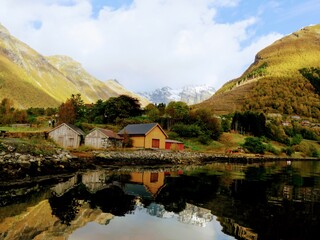 Obraz premium Wooden cabins reflecting on the water amongst the fjords, Urke, Norway