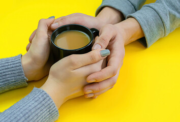 Hands on a yellow background with coffee, love. Coffee with milk, black cup. Selective focus.