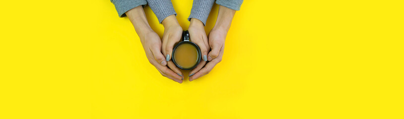 Hands on a yellow background with coffee, love. Coffee with milk, black cup. Selective focus.