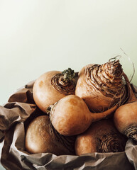 fresh turnips in a crumpled paper bag on a light table. turnip sprigs of greens on a dining table wooden table