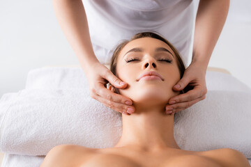 Fototapeta na wymiar female masseur doing facial massage to client in spa salon