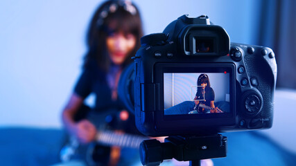 Young woman playing guitar in front of the camera. recording demo or giving online class. High...