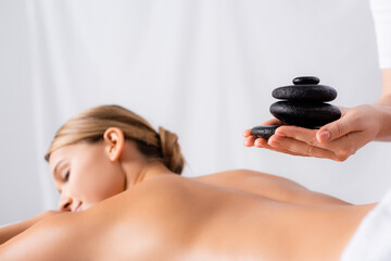 Obraz na płótnie Canvas masseur holding hot stones near client on blurred background