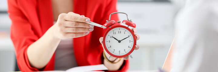 Businesswoman points with pen to colleague at red alarm clock. Time management in business