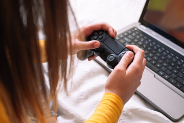 Young woman playing video game with laptop sitting on bed