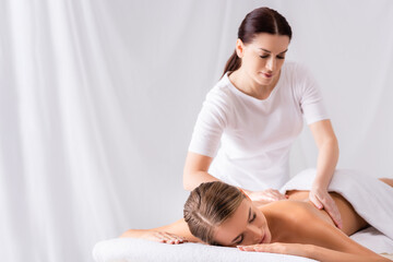 Fototapeta na wymiar Brunette masseur massaging back of woman on massage table in spa salon
