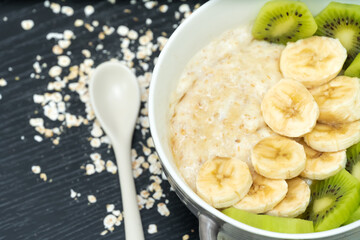 Oatmeal porridge with bananas, kiwi in a bowl on a dark background close-up. Healthy breakfast.