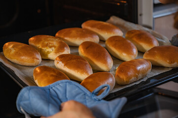 The woman pulls out ready-made Russian pies with filling from the oven. Homemade baking