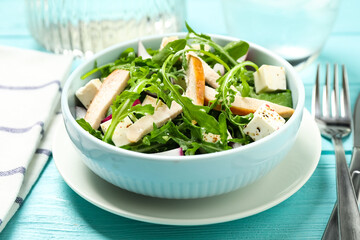 Delicious salad with chicken, arugula and feta cheese on light blue wooden table, closeup