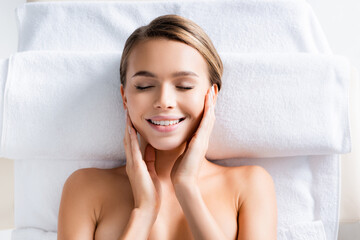 top view of joyful woman with closed eyes lying on massage table in spa salon