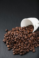 White coffee cup for coffee on the side. A pile of coffee beans on textured black stone. Vertical shooting
