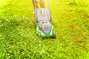 Man cutting green grass with lawn mower in backyard. Gardening country lifestyle background. Beautiful view on fresh green grass lawn in sunlight, garden landscape in spring or summer season.