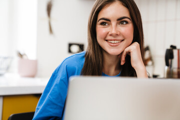 Happy brunette girl working with laptop and smiling at home kitchen