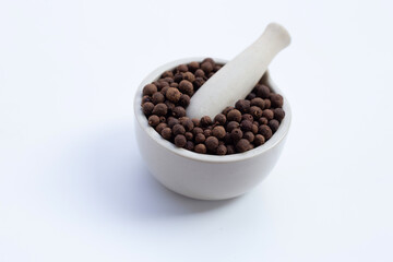 Allspice in porcelain mortar with pestle on white
