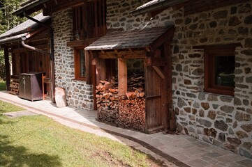 Fototapeta na wymiar A stone house in the mountains with stacked wood logs (Trentino, Italy, Europe)